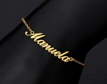 Puede incluir: Pulsera de cadena dorada con el nombre "Manuela" escrito en cursiva.