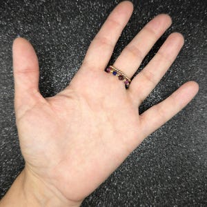 May include: Two gold rings with small, colorful beads are worn on a finger. One ring has a row of small gold beads. The other ring has a row of purple and blue beads. The rings are on a hand.
