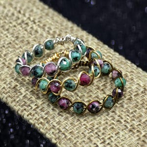 Peut inclure: Trois bagues composées de perles rondes à facettes dans des tons de vert et de rose, chacune entourée d'une spirale continue de fil métallique. Une bague est en fil argenté, tandis que les deux autres sont en fil doré.
