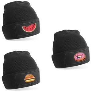 May include: Three black knit beanies with different food patches. The first beanie has a watermelon patch, the second beanie has a doughnut patch, and the third beanie has a hamburger patch.