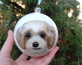 May include: White glass Christmas ornament with a hand-painted portrait of a small, white and brown dog with black eyes.