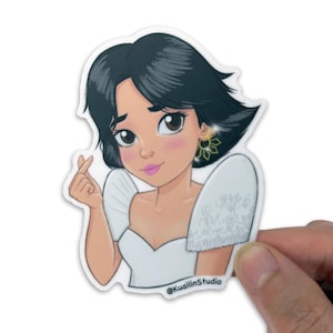 May include: A sticker featuring a cartoon illustration of a woman with dark hair, wearing a white dress with puffed sleeves and a gold earring. The woman is making a heart shape with her fingers. The sticker has the text "@KuallinStudio".