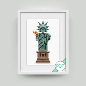 Peut inclure: Un motif de point de croix représentant la Statue de la Liberté, rendu dans un style pixélisé, avec un corps vert, une base brune et une torche orange. Le motif est encadré dans un cadre blanc et étiqueté "PDF" dans le coin inférieur droit.