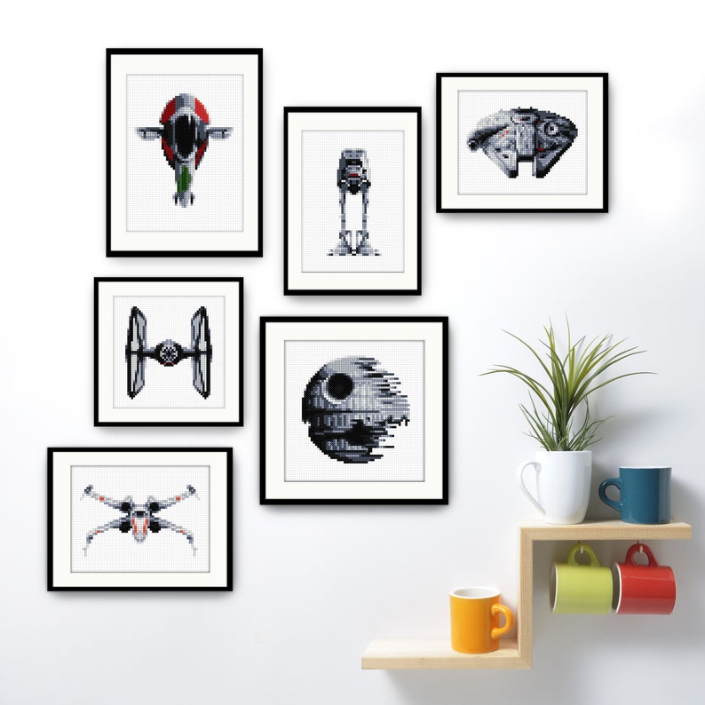 May include: A set of six framed black and white pixel art prints featuring Star Wars characters and vehicles. The prints are displayed on a white wall with a wooden shelf below. The shelf has a potted plant and four mugs.
