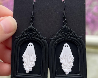 May include: Black polymer clay earrings featuring a white ghost in a black ornate frame. The earrings are on a black card with the text "comet moth co @shopcometmoth".