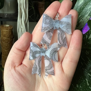 May include: A pair of white bow earrings with a black snake print design.