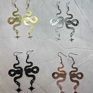 Op de afbeelding: Vier paar slangen oorbellen met een ster bedel. De oorbellen zijn verkrijgbaar in messing, zilver, zwart en ros&eacute; goud.