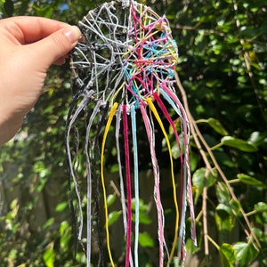 May include: A colorful dreamcatcher with black, white, yellow, pink, and blue string. The dreamcatcher has a circular base with a web-like design and long strings hanging from the bottom.