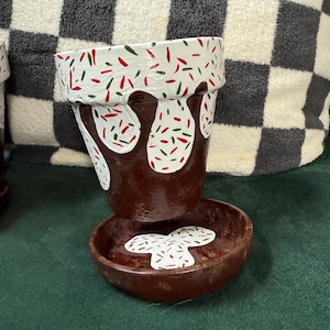 May include: A brown ceramic planter with a white glaze and red and green sprinkles. The planter has a drip effect and is sitting on a matching saucer.