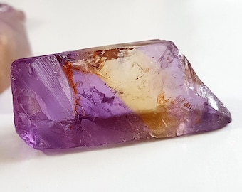 May include: A purple and yellow crystal with a rough, natural shape. The crystal has a translucent appearance with a hint of orange.