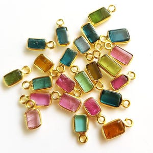 May include: Assortment of colorful gemstone rectangle charms with gold-toned jump rings. The charms feature various shades of green, blue, pink, and brown.