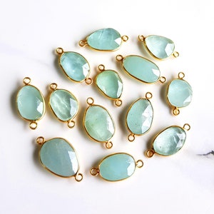 May include: A collection of 12 aquamarine gemstone connector charms with gold-plated jump rings. The stones are faceted and have a light blue color.