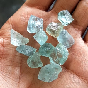 Puede incluir: Una colecci&oacute;n de piedras preciosas de aguamarina azul claro, en bruto y sin cortar, con varias formas y tama&ntilde;os. Las piedras son transl&uacute;cidas y tienen un ligero tono verde.