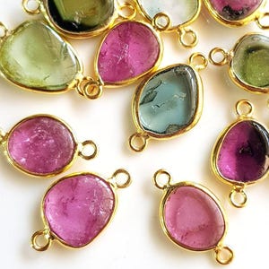 May include: Assortment of gemstone pendants with gold-tone jump rings. The gemstones are in shades of green, pink, and blue.