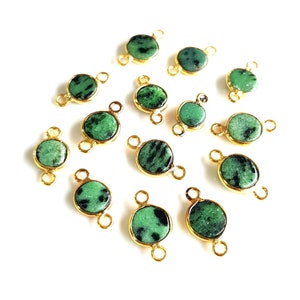 May include: A collection of 14 green gemstone beads with gold-toned jump rings. The beads are round and have a mottled green color. The jump rings are attached to the top and bottom of each bead.