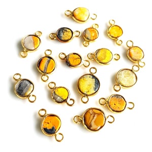 May include: A collection of round gemstone connectors with gold-colored metal settings. The gemstones feature yellow, orange, gray, and white colors. Each connector has two loops for attaching to other jewelry components.