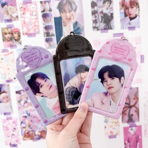 May include: Three K-pop idol photo card holders in purple, black, and pink. Each holder has a heart-shaped top with the text "EMOTIONAL SUPPORT KPOP IDOL." The holders contain photos of K-pop idols.