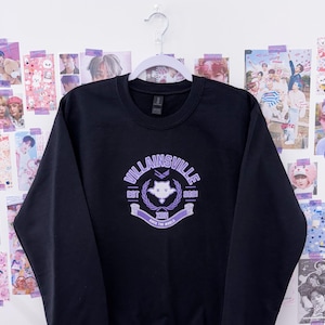 May include: Black crewneck sweatshirt with a purple graphic that reads "Villainsville" with a crest design. The sweatshirt is hanging on a white hanger against a wall decorated with various posters.