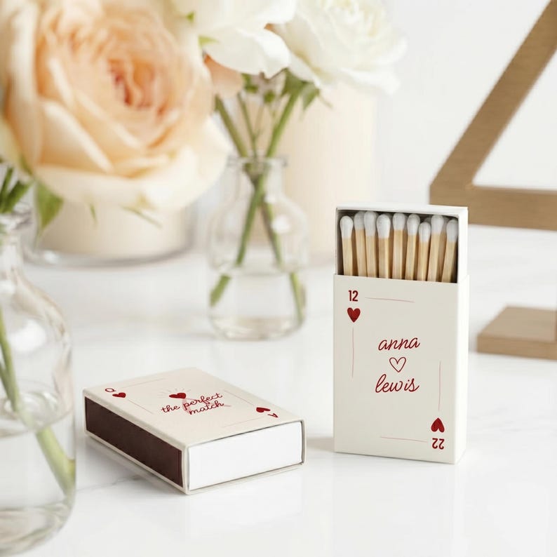 May include: Two matchboxes, one closed and one open, with white matchsticks. The closed box reads "the perfect match" and the open box has the names "anna lewis" and a heart symbol. The boxes have red heart suit symbols.