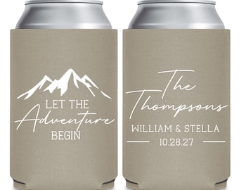 May include: Two beige can coolers with white text and mountain graphics. One cooler reads "Let the Adventure Begin." The other cooler says "The Thompsons" with names and a date. Perfect for a wedding or outdoor event.