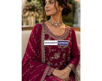May include: A deep magenta long-sleeved tunic featuring intricate gold floral embroidery along the neckline, cuffs, and hem. The garment includes a matching draped shawl with delicate gold stitching and a rectangular label reading DESIGNER HARSHA.