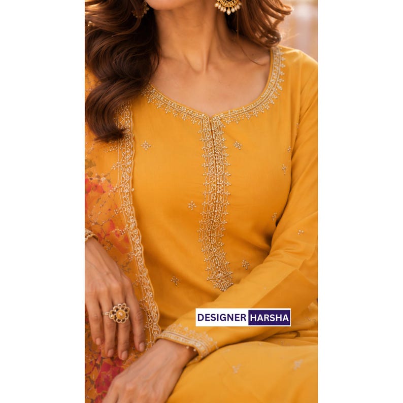 Puede incluir: Una t&uacute;nica de color amarillo mostaza de manga larga con intrincados bordados dorados a lo largo del cuello redondo y un panel central vertical. La prenda incluye un chal a juego con estampado floral transparente. El texto dice DESIGNER HARSHA.