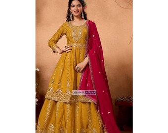 May include: Mustard yellow long-sleeved dress with intricate gold embroidery and embellishments. A vibrant red dupatta is draped over the shoulder. The dress features a tiered skirt and is labeled "DESIGNER HARSHA".