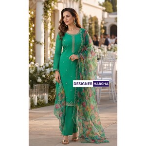 Puede incluir: Un conjunto de t&uacute;nica verde esmeralda de manga larga y pantal&oacute;n a juego con delicados bordados plateados en el cuello y el dobladillo. Un dupatta ligero y transparente con estampado floral colorido cuelga del hombro. El texto dice DESIGNER HARSHA.