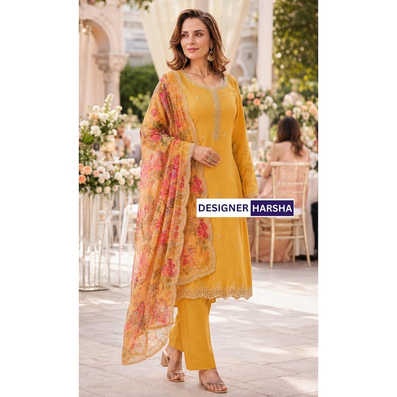 Puede incluir: Un conjunto de t&uacute;nica de manga larga y pantal&oacute;n color amarillo mostaza con bordados intrincados en el cuello y el dobladillo. Un dupatta transparente con estampado floral y bordes festoneados cuelga del hombro. El texto DESIGNER HARSHA es visible.