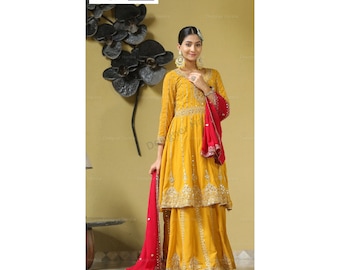 Può includere: Una tunica giallo senape a maniche lunghe e una gonna abbinata con intricati ricami argentati e decorazioni a specchio. Il completo include una dupatta rosso vivace con un bordo decorativo. Il testo Designer Harsha è visibile.