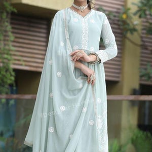 May include: A light blue embroidered dress with a matching dupatta. The dress has a V-neckline and a long, flowing skirt. The dupatta is decorated with white floral embroidery. The dress is worn by a woman with long, dark hair and a necklace.