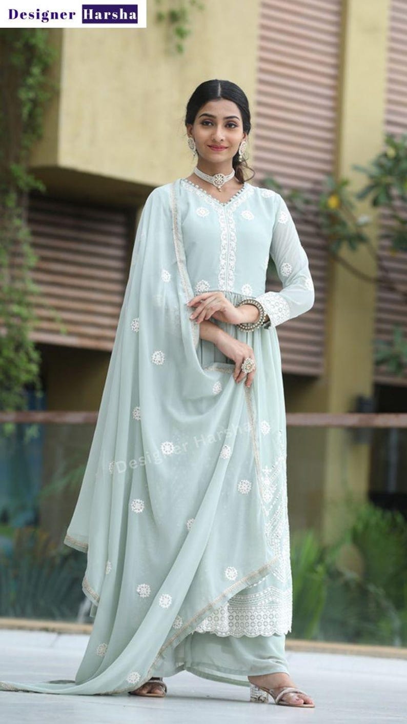 May include: A light blue embroidered dress with a matching dupatta. The dress has a V-neckline and a long, flowing skirt. The dupatta is decorated with white floral embroidery. The dress is worn by a woman with long, dark hair and a necklace.