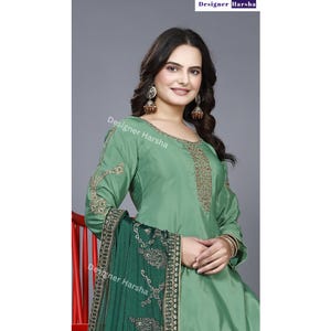 May include: A green salwar kameez with gold embroidery. The kameez has long sleeves and a round neckline. The salwar is a pair of loose-fitting pants. The outfit is paired with a green dupatta with gold embroidery.