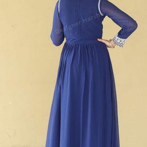 May include: A long, royal blue maxi dress with a high neckline and long sleeves. The dress has a gathered waist and a flowing skirt. The dress is decorated with silver embroidery around the neckline and cuffs.