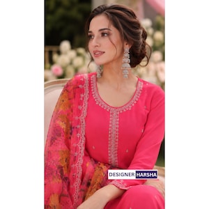 Puede incluir: Una t&uacute;nica de color rosa brillante de manga larga con intrincados bordados plateados a lo largo del escote y el panel central, combinada con una dupatta floral transparente a juego en tonos rosa, naranja y amarillo. El texto DESIGNER HARSHA es visible.