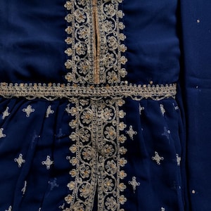 Op de afbeelding: Een diepblauw kledingstuk met ingewikkeld goudborduursel langs het middenpaneel en de taille. De stof is versierd met kleine, herhalende goudkleurige kruisvormige motieven. Een label bovenaan in het midden toont de tekst DESIGNER HARSHA.