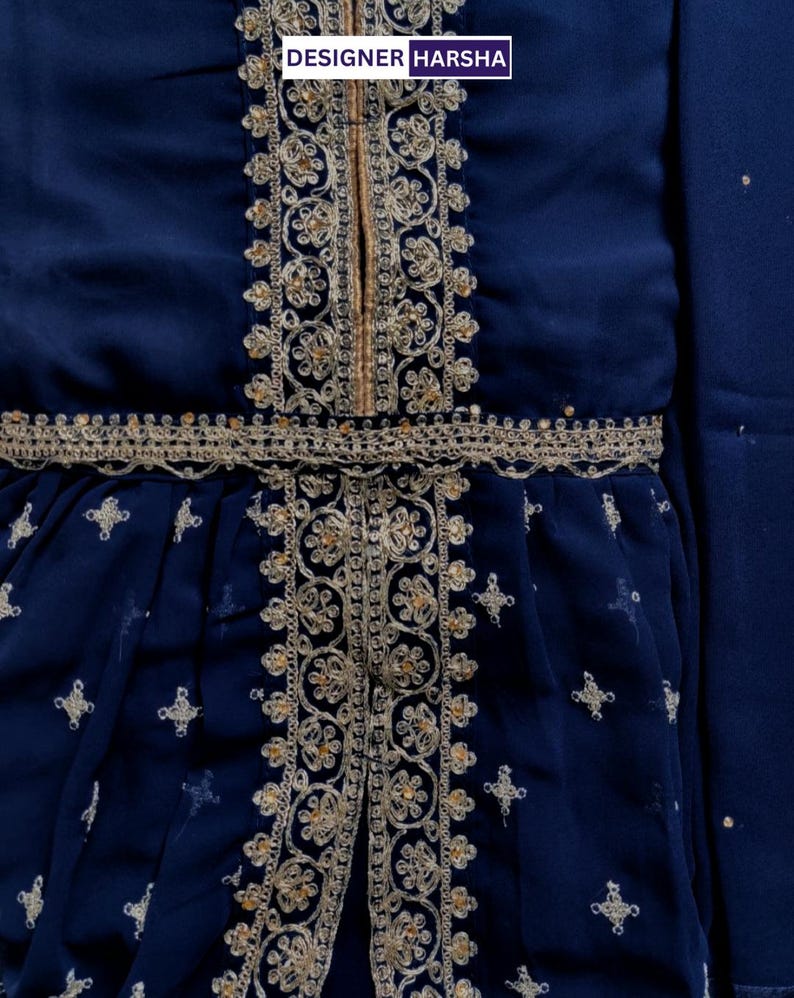 Op de afbeelding: Een diepblauw kledingstuk met ingewikkeld goudborduursel langs het middenpaneel en de taille. De stof is versierd met kleine, herhalende goudkleurige kruisvormige motieven. Een label bovenaan in het midden toont de tekst DESIGNER HARSHA.