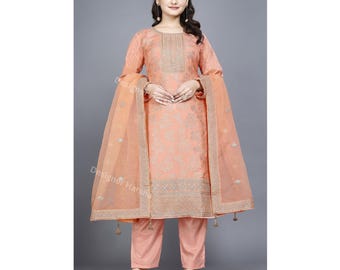 May include: Peach colored salwar kameez with a floral pattern and gold embroidery. The outfit includes a long-sleeved top, pants, and a sheer dupatta.