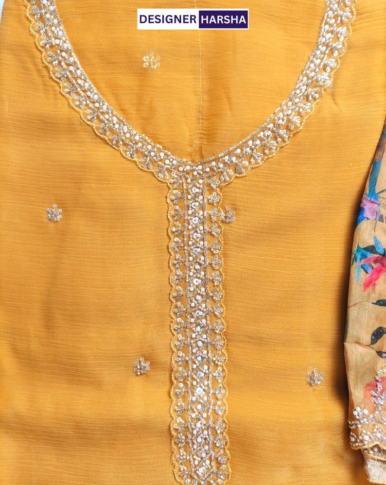 Puede incluir: Una t&uacute;nica de color amarillo mostaza con escote redondo y un panel central vertical adornado con lentejuelas y cuentas plateadas. La tela tiene un acabado texturizado con peque&ntilde;os adornos florales dispersos. El texto DESIGNER HARSHA es visible.