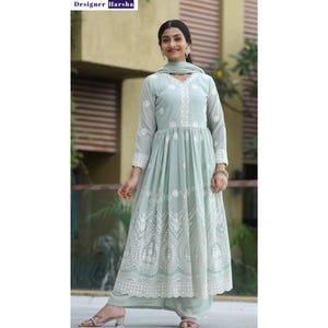 May include: A light green, long-sleeved dress with white embroidery and a matching dupatta. The dress has a gathered skirt and a round neckline. The model is wearing the dress with a pair of silver earrings and a silver bracelet.