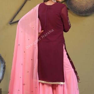 May include: A maroon and pink salwar kameez with embroidery. The kameez is long-sleeved and has a high neckline. The salwar is wide-legged and the dupatta is pink with embroidery. The outfit is made of a soft, flowing fabric.