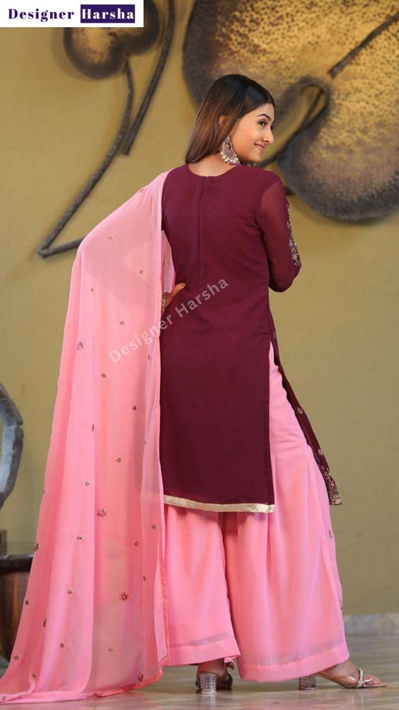 May include: A maroon and pink salwar kameez with embroidery. The kameez is long-sleeved and has a high neckline. The salwar is wide-legged and the dupatta is pink with embroidery. The outfit is made of a soft, flowing fabric.