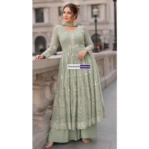 May include: A sage green floor-length dress with long sleeves, featuring intricate white embroidery and reflective mirror embellishments throughout the bodice and skirt. The garment includes a matching scarf and wide-leg trousers. Text reads DESIGNER HARSHA.