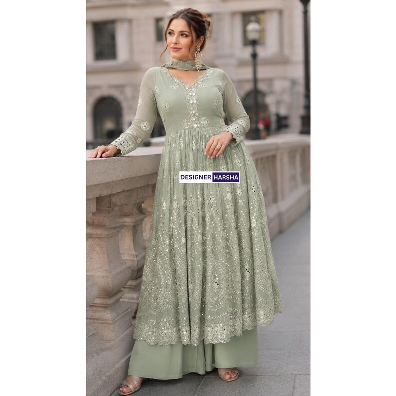 May include: A sage green floor-length dress with long sleeves, featuring intricate white embroidery and reflective mirror embellishments throughout the bodice and skirt. The garment includes a matching scarf and wide-leg trousers. Text reads DESIGNER HARSHA.