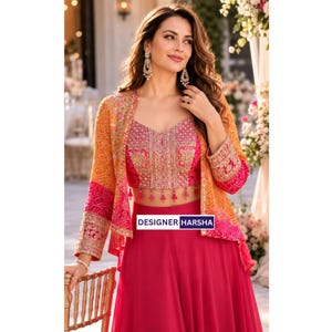 May include: A vibrant three-piece ensemble featuring a solid hot pink floor-length skirt and a matching cropped bodice with intricate gold embroidery and small pink tassels. An orange and pink patterned jacket with gold trim completes the look.