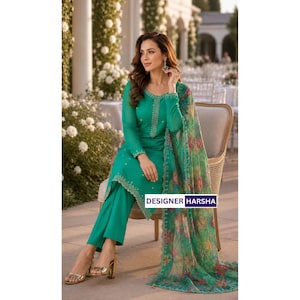 Puede incluir: Un conjunto de t&uacute;nica de manga larga y pantal&oacute;n en color verde esmeralda vibrante con intrincados bordados plateados en el cuello y el dobladillo. Un dupatta transparente con estampado floral en tonos verdes, rosas y amarillos cuelga del hombro. El texto dice DESIGNER HARSHA.
