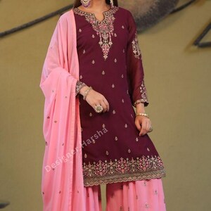 May include: A maroon and pink salwar kameez with gold embroidery. The kameez has a long-sleeved design and the salwar is a wide-legged pant. The outfit is paired with a pink dupatta.