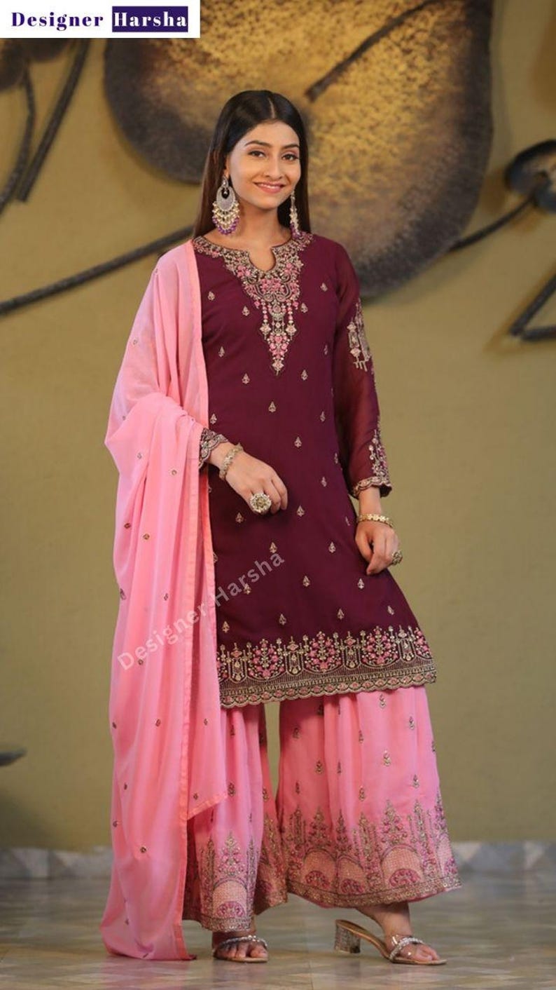 May include: A maroon and pink salwar kameez with gold embroidery. The kameez has a long-sleeved design and the salwar is a wide-legged pant. The outfit is paired with a pink dupatta.