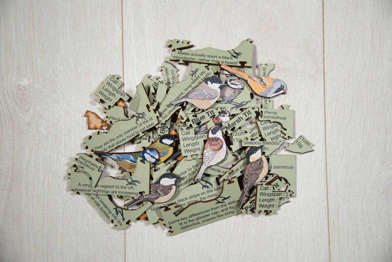 May include: A wooden jigsaw puzzle of different types of birds, including a blue tit, a marsh tit, and a great tit. The puzzle pieces are scattered on a light wood surface. Each piece has a bird illustration and information about the bird, such as its call, wingspan, length, and weight.