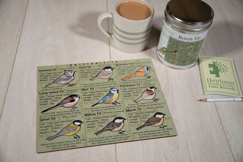 May include: A wooden puzzle featuring illustrations of different British tit birds, including the Crested Tit, Long-tailed Tit, Great Tit, Coal Tit, Blue Tit, Willow Tit, Bearded Tit, Penduline Tit, and Marsh Tit. Each bird is labeled with its name, call, wingspan, length, and weight in inches and grams. The puzzle is part of a collection called "British Tits" and is made by Heirloom Wooden Puzzles.